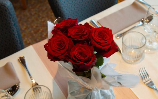 Table décorée avec un bouquet de roses rouges pour un dîner croisière romantique sur la Seine à Paris, offrant une vue sur un pont emblématique | Le Capitaine Fracasse