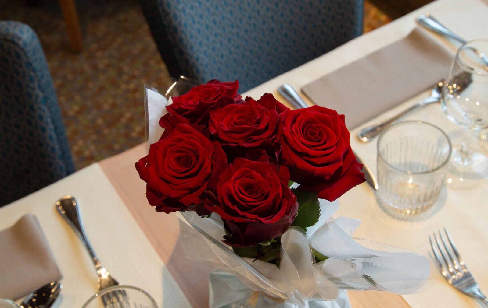 Table décorée avec un bouquet de roses rouges pour un dîner croisière romantique sur la Seine à Paris, offrant une vue sur un pont emblématique | Le Capitaine Fracasse